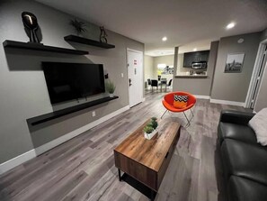 Een moderne woonkamer met een flatscreen televisie, een houten salontafel, een zwarte leren bank en een rode fauteuil.