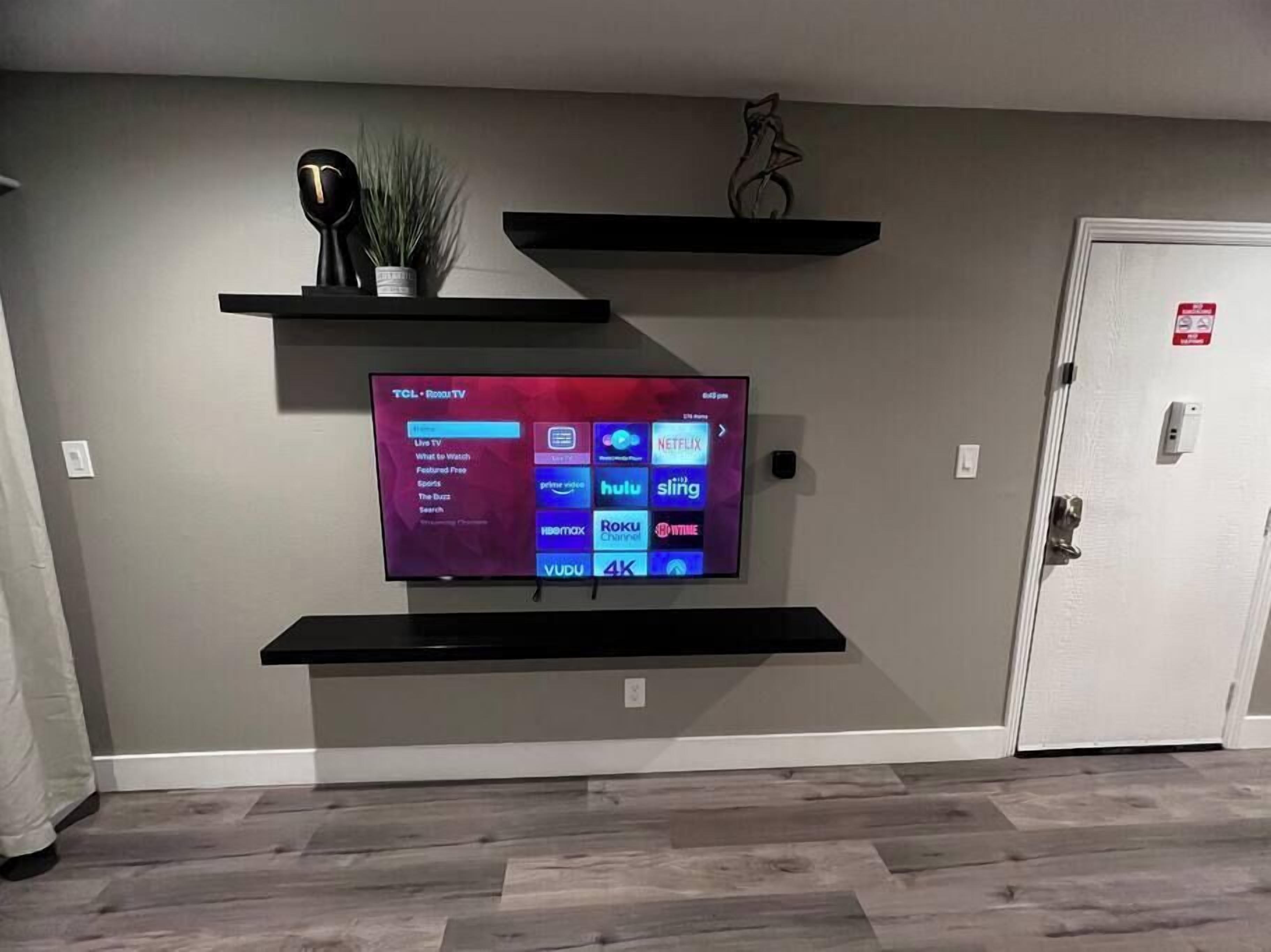 A flat-screen TV mounted on a wall with a digital interface displaying various streaming services.