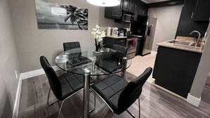 A modern kitchen with dark cabinetry, a stainless steel refrigerator, and a glass dining table with black chairs. - Dune Suite 2b/1b fully furnished (Las Vegas)
