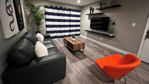 A modern living room with a black leather sofa, a wooden coffee table, and an orange chair. - Dune Suite 2b/1b fully furnished (Las Vegas)