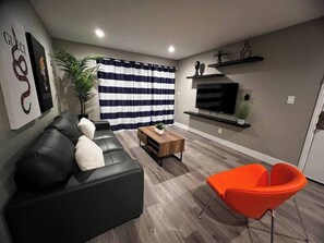 Ein modernes Wohnzimmer mit einer schwarzen Ledersofa, einem Holztisch und einem orangefarbenen Sessel.