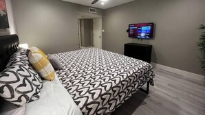 Ein Schlafzimmer mit einem Bett, einem Deckenventilator, einem an der Wand befestigten Fernseher und einer Tür zu einem weiteren Raum.