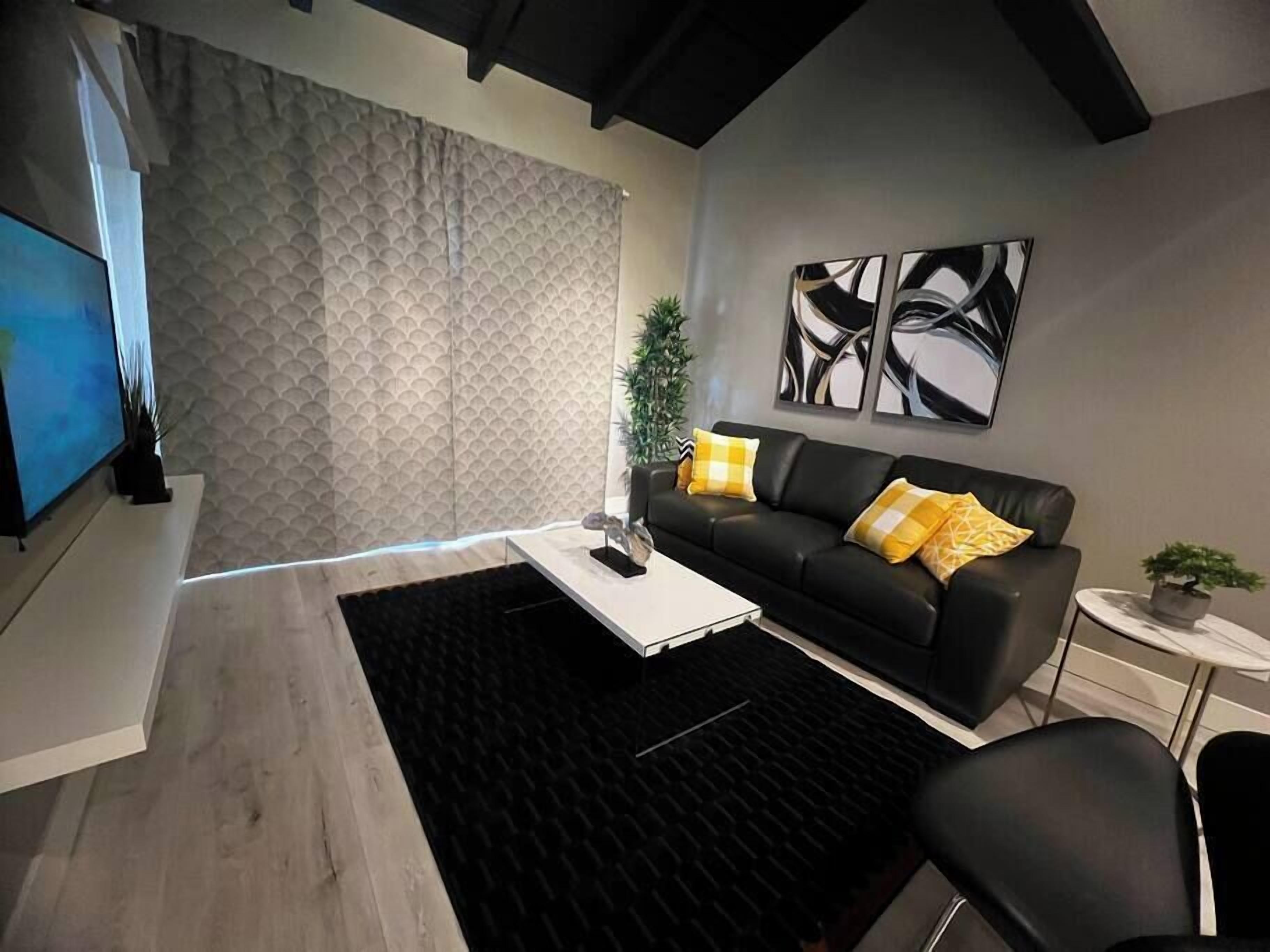 Un salon moderne avec un canapé en cuir noir, une table basse blanche et un tapis noir.