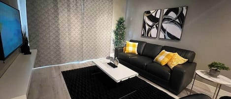 Un salon moderne avec un canapé en cuir noir, une table basse blanche et un tapis noir.