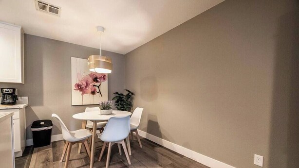 Een eetgedeelte met een ronde tafel, vier stoelen, een hanglamp en een schilderij aan de muur.