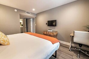 Habitación de hotel con cama, escritorio, silla, televisor y puerta que da a un baño.