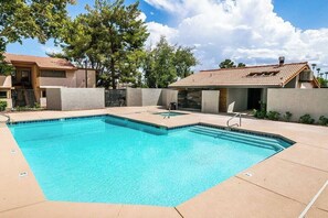 Ein rechteckiger Swimmingpool mit einer gefliesten Terrasse, umgeben von einer niedrigen Mauer und Bäumen.