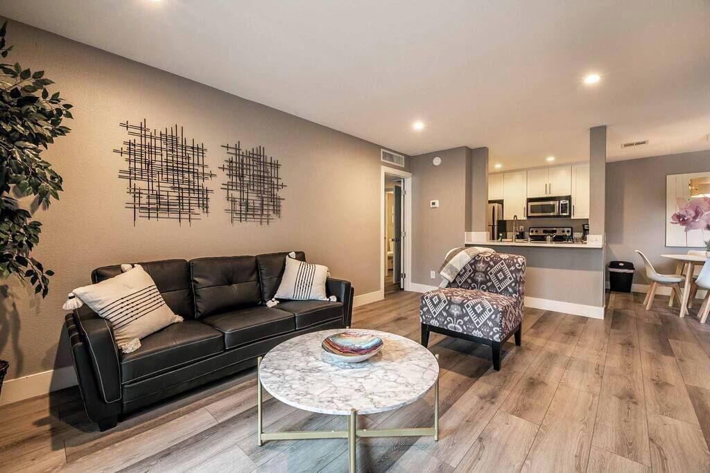 A modern living room with a black leather sofa, a patterned armchair, and a marble coffee table.