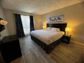 Ein Hotelzimmer mit Bett, Nachttischlampen, einem Gemälde und einem Schreibtisch.