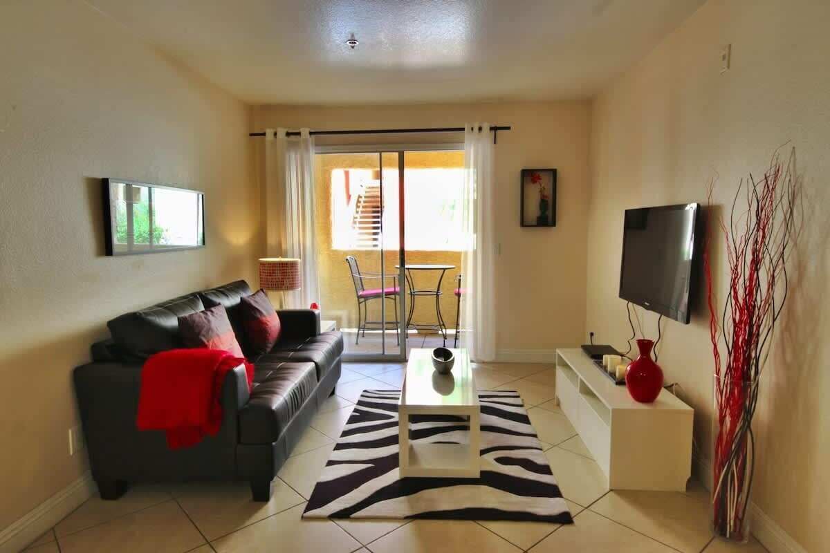 Un salón con sofá, mesa de centro, televisor y puerta corrediza de vidrio que da a un balcón.