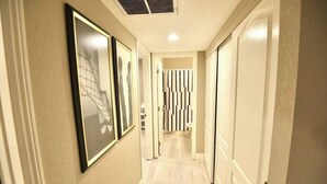 A hallway with framed artwork on the walls, a light-colored floor, and a door at the end. - Apex suite 2b/2b entire condo ! (Las Vegas)