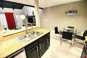 Een moderne keuken met een dubbele spoelbak, zwarte kastjes en een eethoek met een glazen tafel en zwarte stoelen.