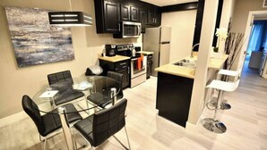 A modern kitchen with black cabinets, stainless steel appliances, and a dining area with a glass table and black chairs. - Apex suite 2b/2b entire condo ! (Las Vegas)