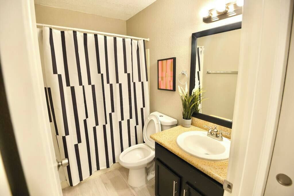 Un bany amb vàter, un lavabo, un mirall i una cortina de bany amb un dibuix geomètric.