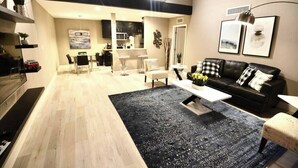 A modern living room with a black sofa, a coffee table, and a dining area with chairs. - Apex suite 2b/2b entire condo ! (Las Vegas)