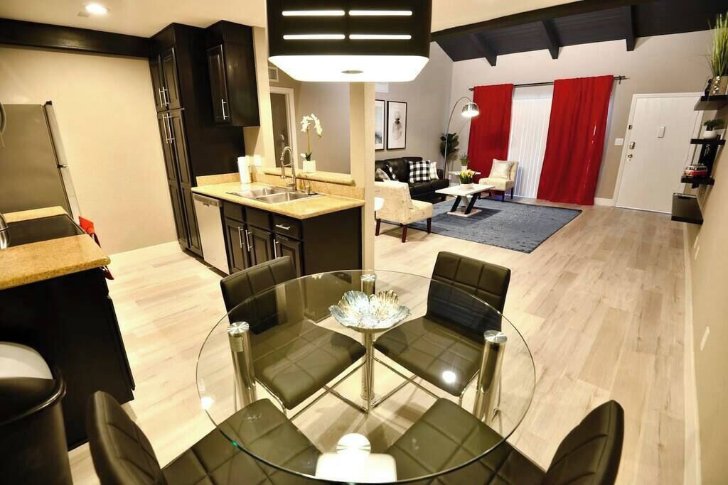 Una cocina moderna con comedor, una sala de estar con cortinas rojas y una puerta visible.
