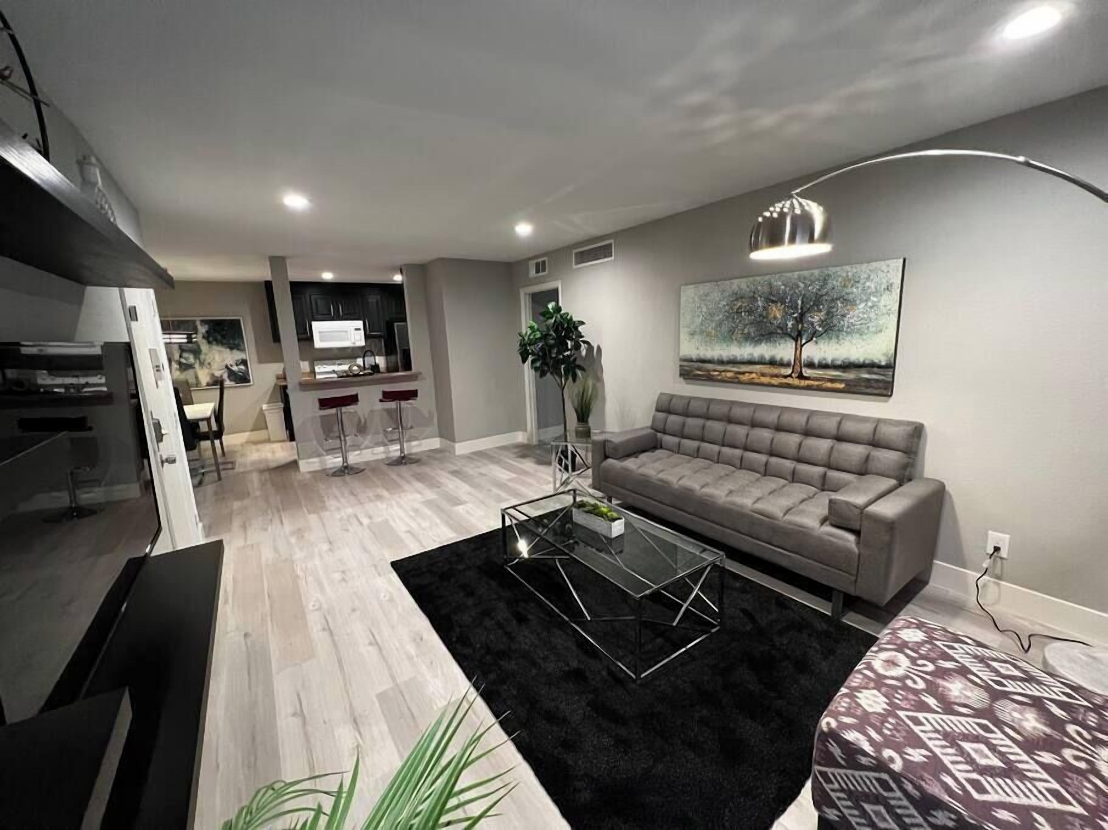 Un salon moderne avec un canapé gris, une table basse en verre et un tapis noir.