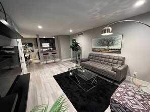 Ein modernes Wohnzimmer mit einem grauen Sofa, einem Glastisch und einem schwarzen Teppich.