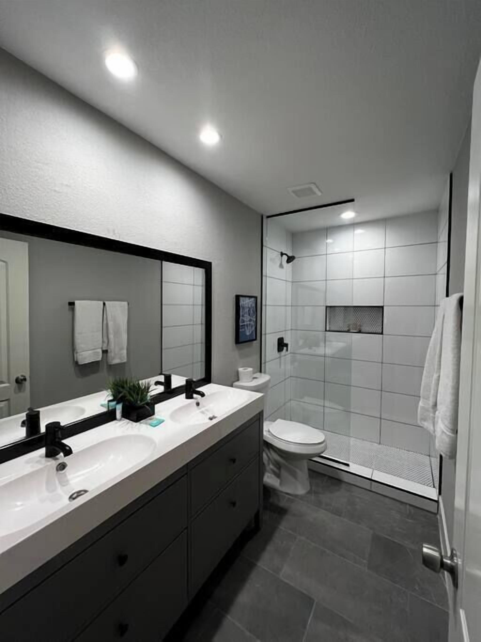 A modern bathroom with a dual sink vanity, a toilet, and a shower enclosure.