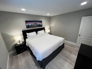 A bedroom with a large bed, bedside tables, a nightstand, a painting on the wall, and a door. - Alpine Suite 2 Bed/1 Bath (Las Vegas)