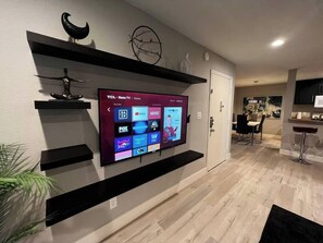 A modern living room with a flat-screen TV mounted on a wall, wooden flooring, and a minimalist decor style. - Alpine Suite 2 Bed/1 Bath (Las Vegas)