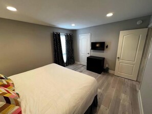Ein Schlafzimmer mit einem Bett, einem Fernseher, einer Tür und einem Fenster mit Vorhängen.