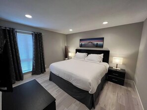 A modern bedroom with a large bed, bedside tables, and a window with curtains. - Alpine Suite 2 Bed/1 Bath (Las Vegas)