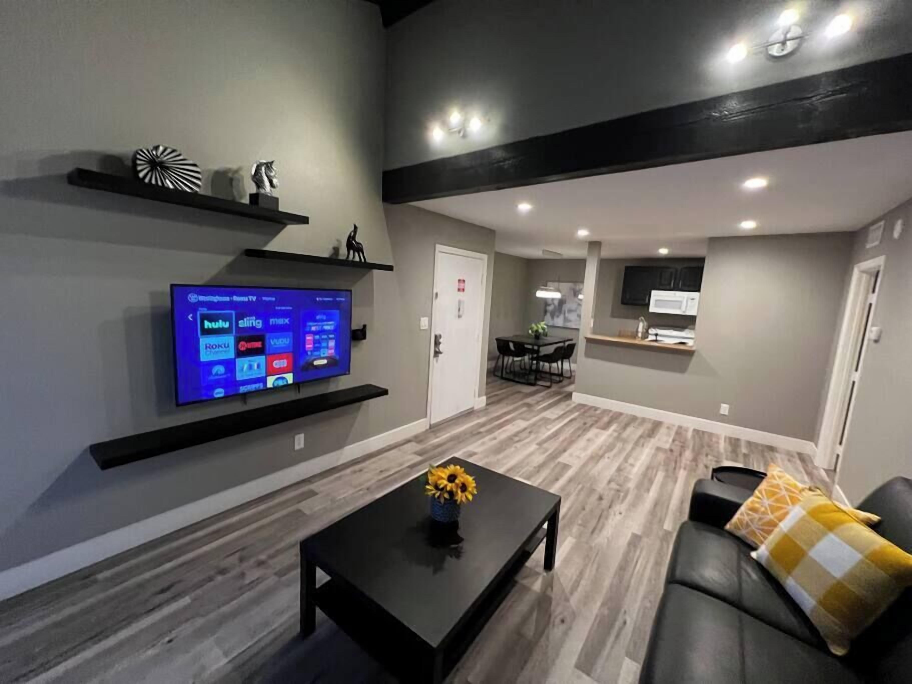 A modern living room with a flat-screen TV, a coffee table with a vase, and a sofa with a throw pillow.