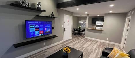 Una sala de estar moderna con un televisor de pantalla plana, una mesa de centro con un florero y un sofá con un cojín decorativo.