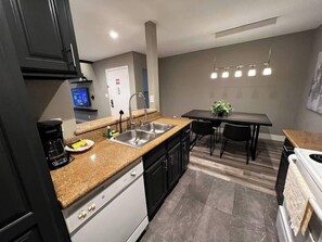 A modern kitchen with granite countertops, a double sink, and a dining area with a table and chairs. - Noma Suite Entire 2bed/2bath (Las Vegas)