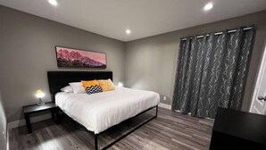 Een slaapkamer met een bed, nachtkastje, lamp en een schilderij aan de muur.