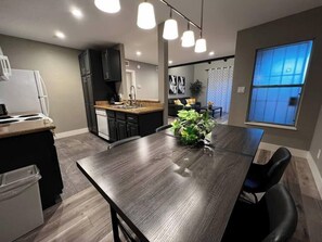 A modern kitchen with a dining area, a refrigerator, a sink, and a window with blue-tinted glass. - Noma Suite Entire 2bed/2bath (Las Vegas)