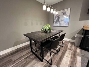 A modern dining area with a wooden table and chairs, a hanging light fixture, and a wall-mounted abstract painting. - Noma Suite Entire 2bed/2bath (Las Vegas)