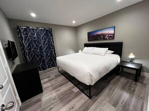 A bedroom with a bed, a nightstand, a black cabinet, a cityscape painting, and a patterned curtain. - Noma Suite Entire 2bed/2bath (Las Vegas)
