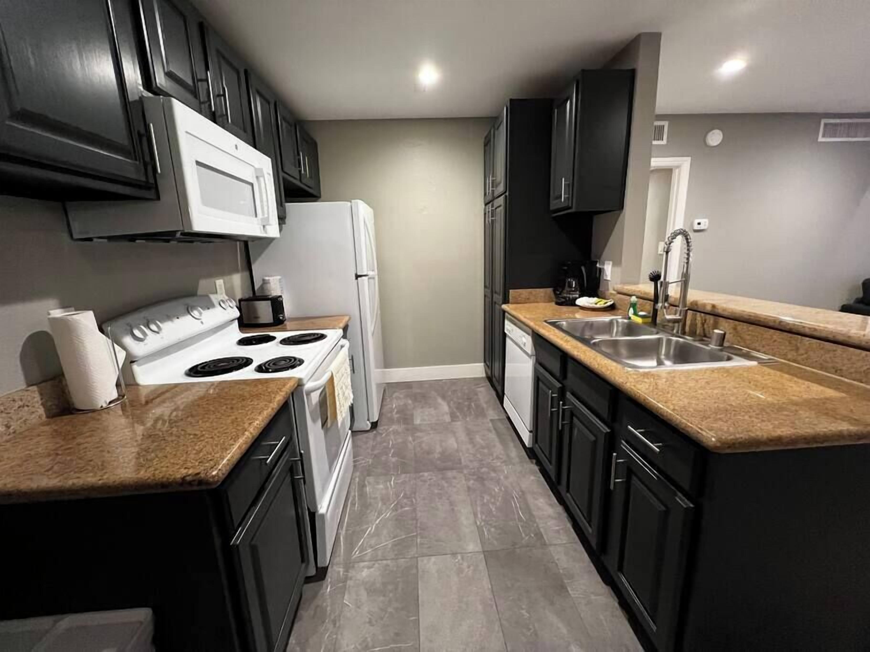 A kitchen with black cabinets, a white stove, a white refrigerator, a granite countertop, and a stainless steel sink.