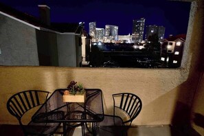 A balcony with a table and chairs, overlooking a city skyline at night. - Chelsea Suite 2b/2b Strip View! (Las Vegas)