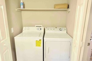 A laundry room with two white washing machines and a shelf above them. - Chelsea Suite 2b/2b Strip View! (Las Vegas)