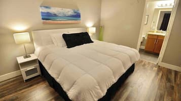 A bedroom with a bed, nightstands, a painting, and a bathroom visible through an open door.