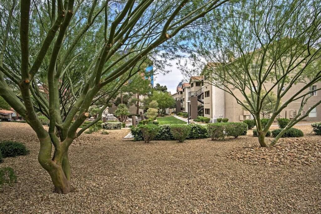 A building with multiple floors, surrounded by a gravel courtyard with trees and shrubs.