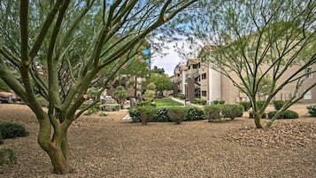 A building with multiple floors, surrounded by a gravel courtyard with trees and shrubs.