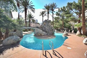 A pool area with a stone bridge, lounge chairs, and palm trees. - Chelsea Suite 2b/2b Strip View! (Las Vegas)
