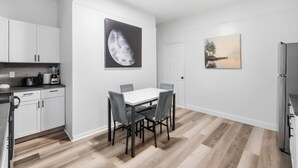 A modern kitchen with white cabinets, a dining table with chairs, and artwork on the walls. - Peaceful Dayton Cottage Near Downtown (Dayton)