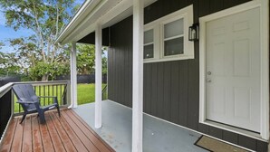 A covered porch with a wooden deck, a white door, and a black chair. - Peaceful Dayton Cottage Near Downtown (Dayton)