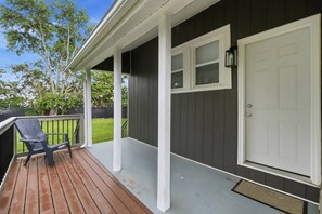 Eine überdachte Veranda mit Holzterrasse, einer weißen Tür und einem schwarzen Stuhl.