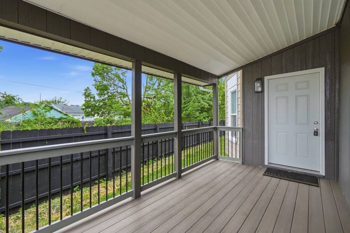 A covered porch with a wooden floor, a black railing, and a white door.