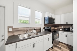 A modern kitchen with white cabinets, a double sink, a stove, and a microwave. - Peaceful Dayton Cottage Near Downtown (Dayton)