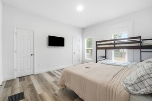 Une chambre avec un lit superposé, un téléviseur à écran plat fixé au mur et une fenêtre avec des stores.