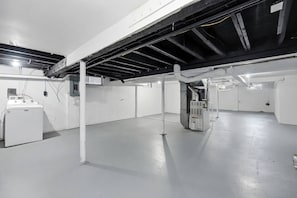 Una habitación amplia de estilo industrial con vigas a la vista, una lavadora grande y una unidad de aire acondicionado central.