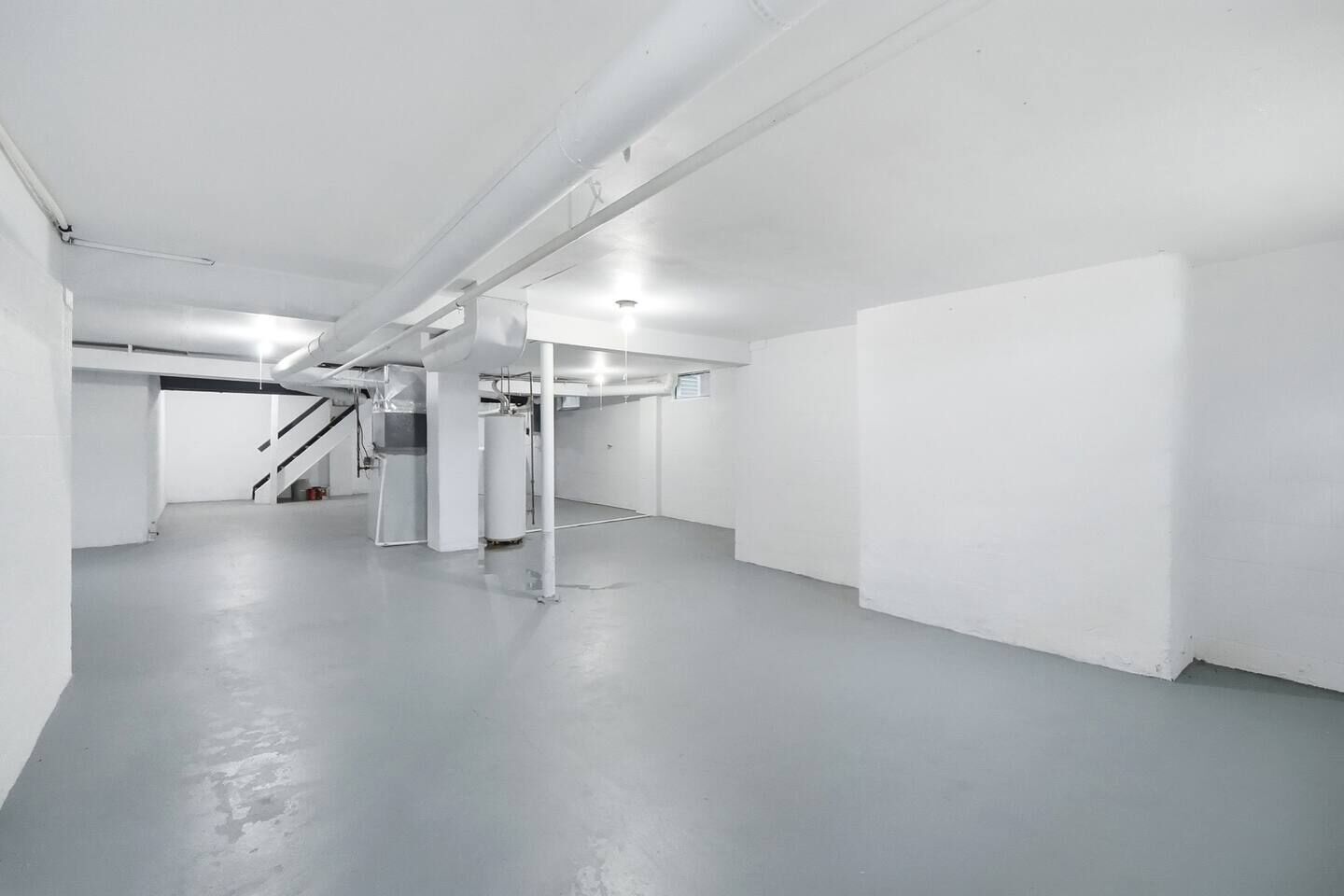 Ein geräumiger, heller Innenraum mit Betonboden, sichtbaren Stahlträgern und einer Treppe, die in ein Obergeschoss führt.