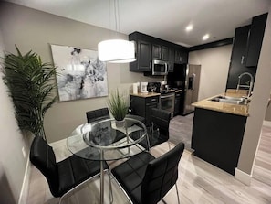 A modern kitchen with black cabinets, stainless steel appliances, and a glass dining table with black chairs. - Eden Suite 2b/2b fully furnished (Las Vegas)